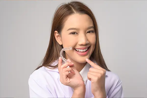 Teen Asian girl holding and pointing to a pair of clear aligners