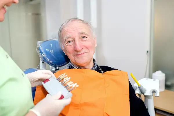 A dentist consults a shade match with a senior patient during a dental care visit.